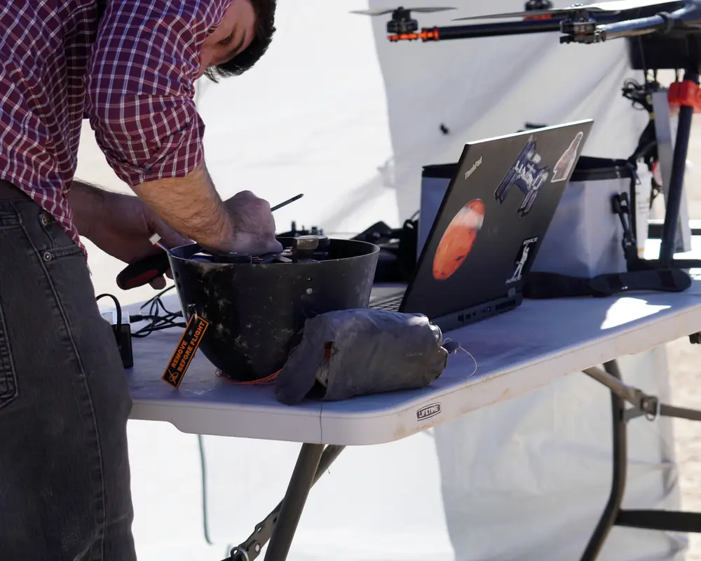 An engineer preparing a pod on a field table beside a drone