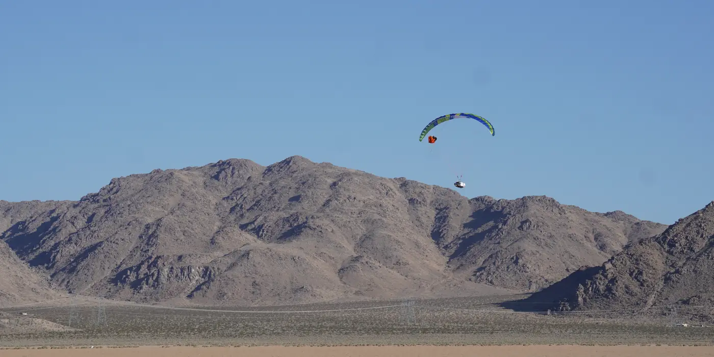 A test glider flying past desert mountains